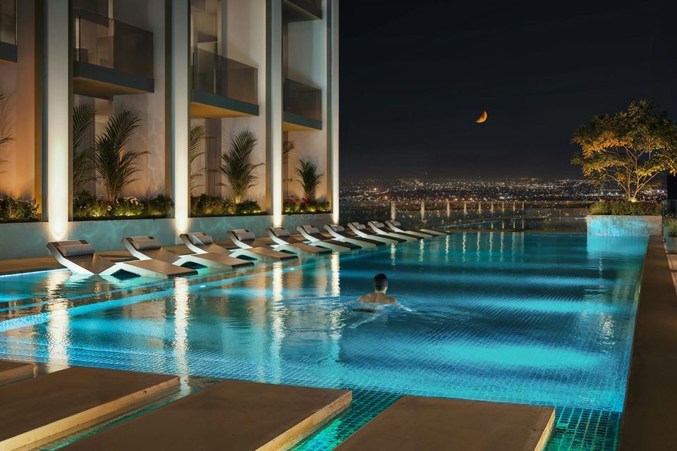 Podium pool lit at night with loungers along the edge