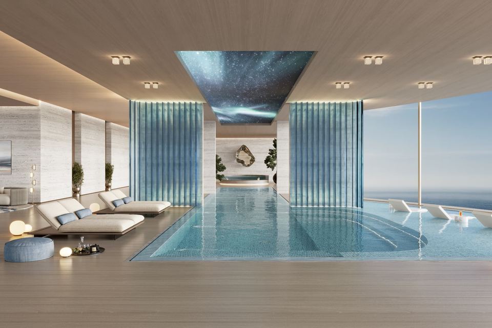 Indoor pool with loungers and a wall of glass looking out to the sea